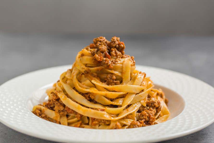 A white plate with tagliatelle al ragù in it, or spaghetti bolognese.