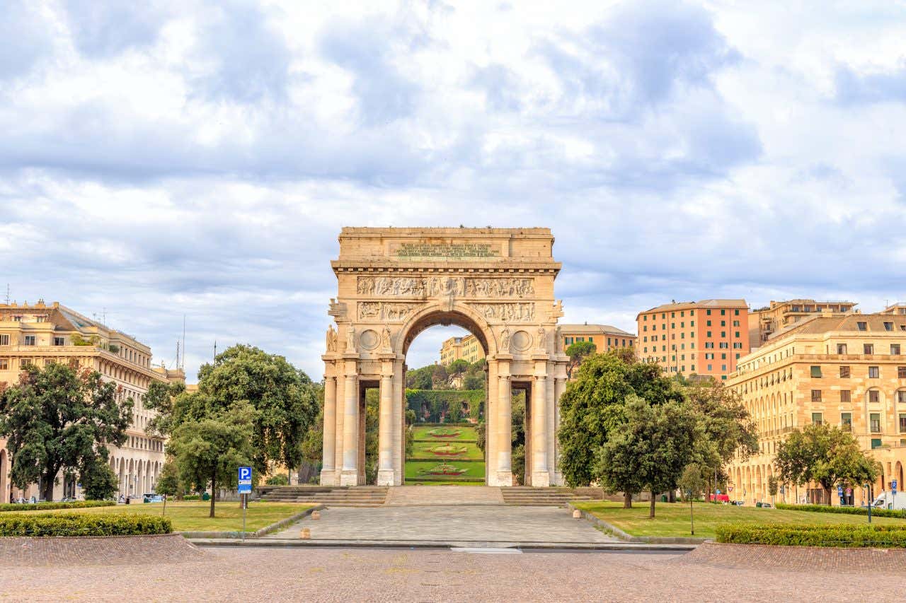 Um grande arco de mármore branco sustentado por colunas e, ao fundo, uma escadaria de jardins com decorações florais, uma das atrações que ver em Gênova