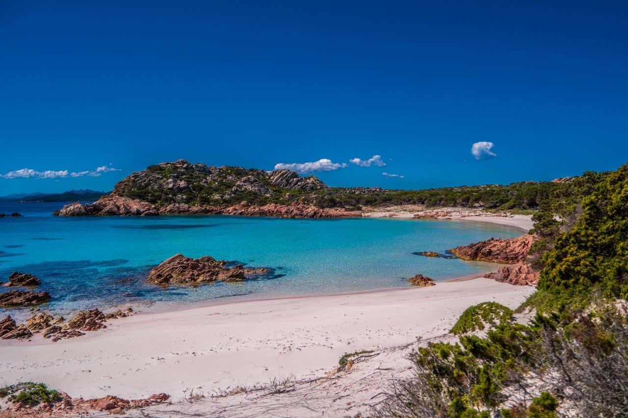 Una caletta di sabbia di colore rosa bagnata dalle acque pulite e azzurre del mare in un giorno di sole senza nuvole