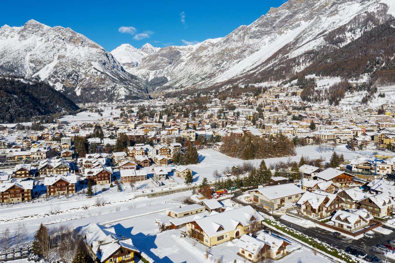 Vista di un piccolo paesino di montagna ricoperto di neve di una giornata di sole e con diverse montagne innevate sullo sfondo