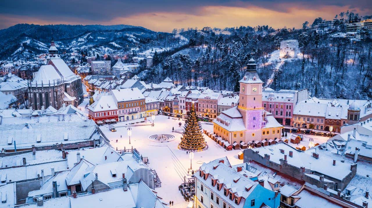 Il centro di un paese di montagna di sera illuminato da diverse luci e con un albero di natale al centro della piazza