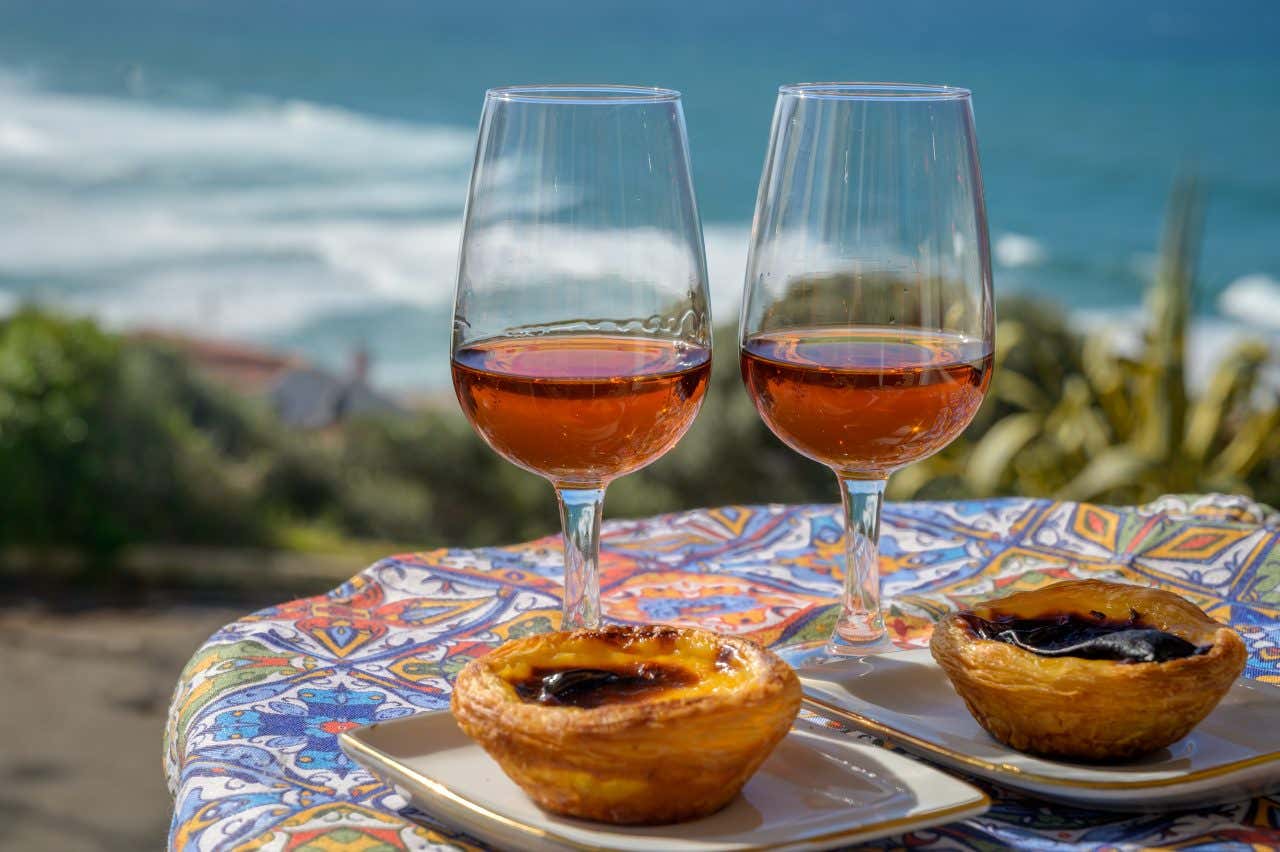 Deux verres de Porto sur une table avec deux pasteis de nata devant et la mer en fond