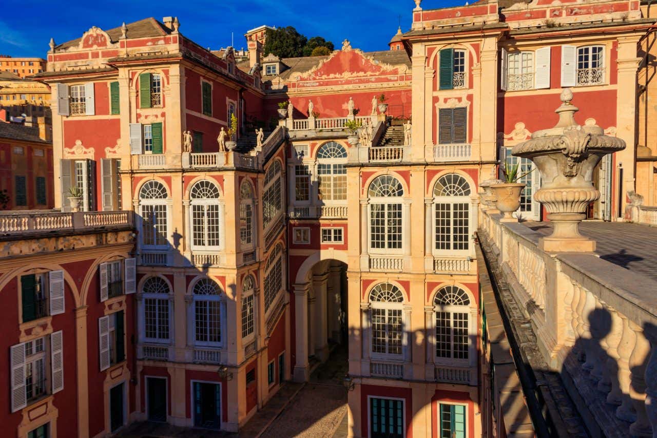 A fachada, fotografada de cima, de um enorme palácio situado no centro de Gênova. Ele é decorada com grandes vitrais, arcos, estátuas e vasos de pedra