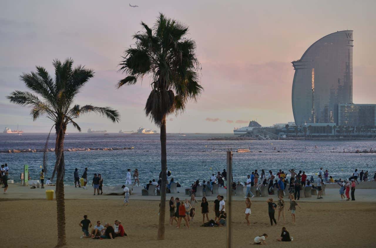 Barceloneta beach, with lots of people on the sand, and some buildings visible across the water.