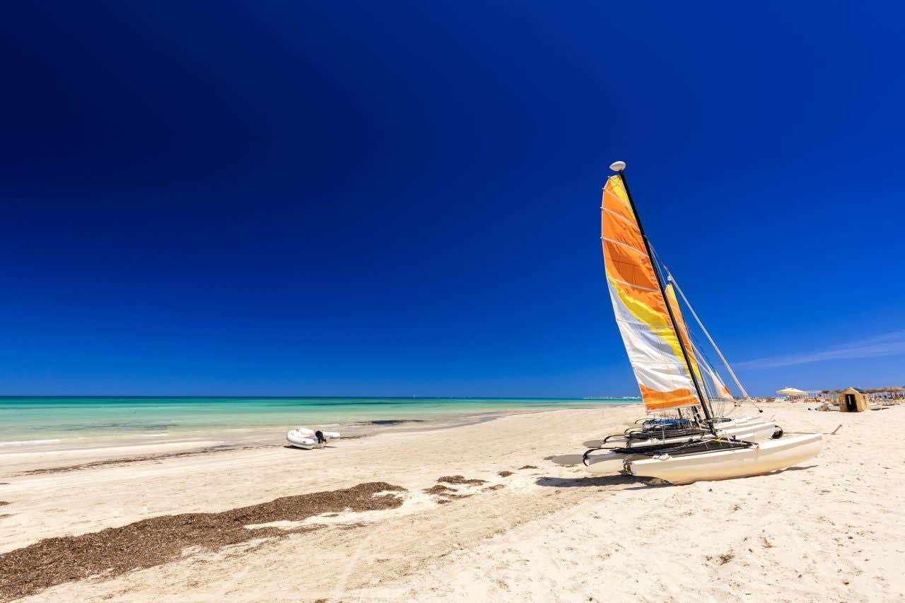 Una barca a vela abbandonata sul bagnasciuga della baia di Djerba a Tunisi. Il cielo è di un azzurro intenso e privo di nuvole 