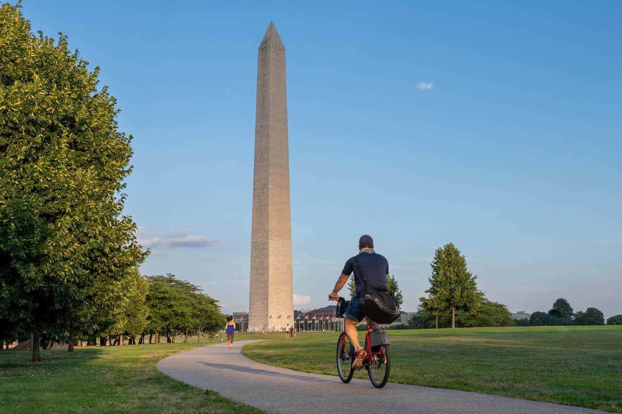 A man biking in Washington DC with the Washington Monument in the background.