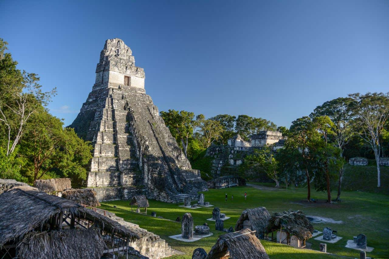 I resti di un antico tempio maya a forma piramidale, all'interno di una giungla verdeggiante in una giornata di sole senza nuvole