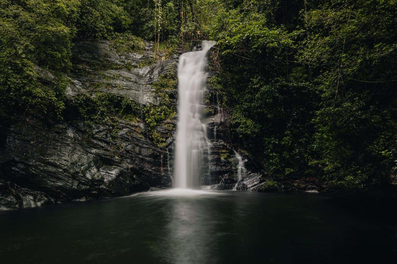 Maya King Waterfalls in Belize as seen from across the water, with rock and vegetation on either side of the water.