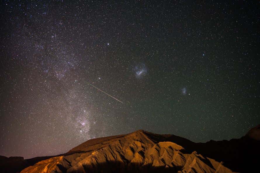 La Vía Láctea sobre el desierto de Atacama donde se ven unas formaciones rocosas debajo