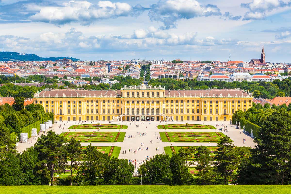 Vista aérea del palacio Schönbrunn, un edificio de color amarillo rodeado por jardines y con varias personas paseado por la zona