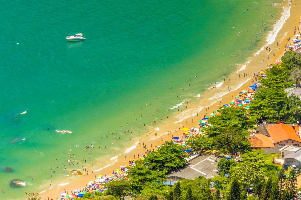 Vista aérea da praia de Laranjeiras com o mar verde e muitos banhistas