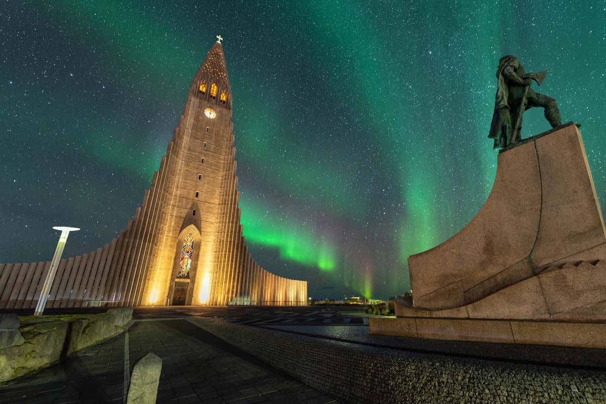 La iglesia de Hallgrímskirkja iluminada por la noche bajo la luz de la aurora boreal y las estrellas, uno de los mejores lugares a donde viajar en febrero