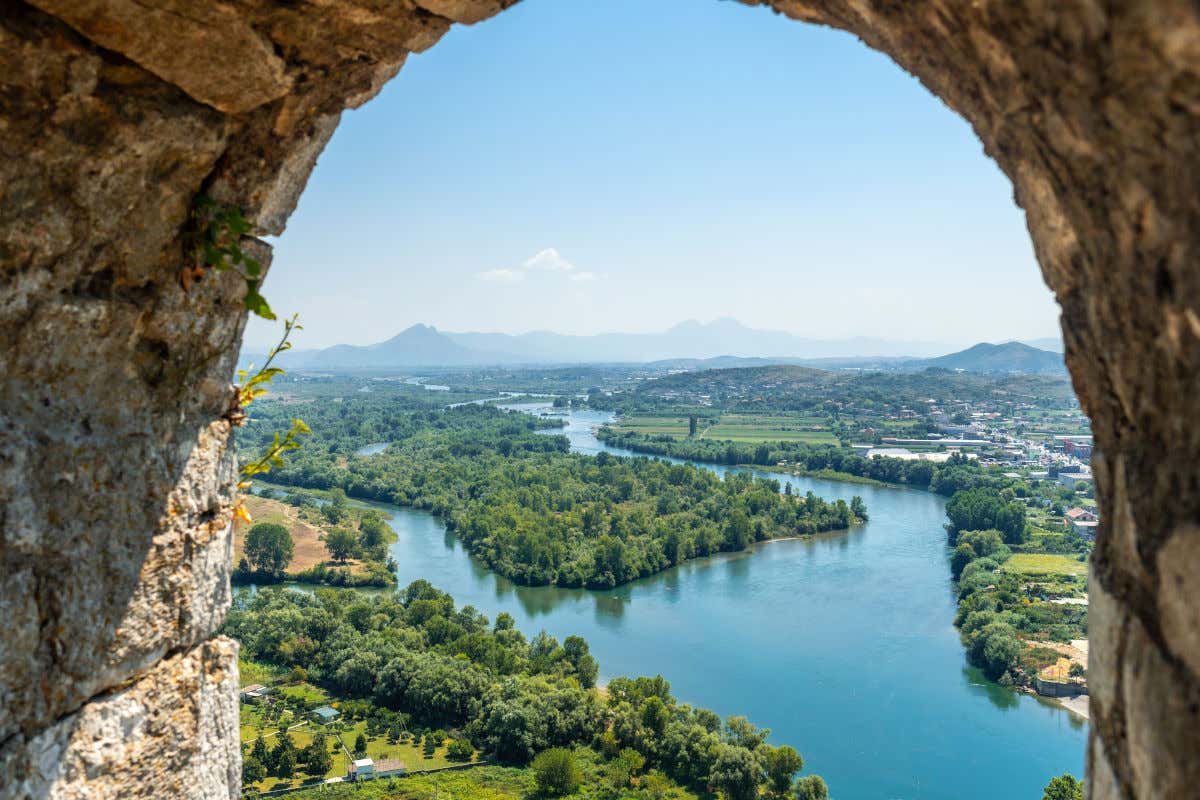 Un arco di pietra di un castello da cui si vedono una città e un fiume circondati dal verde della natura