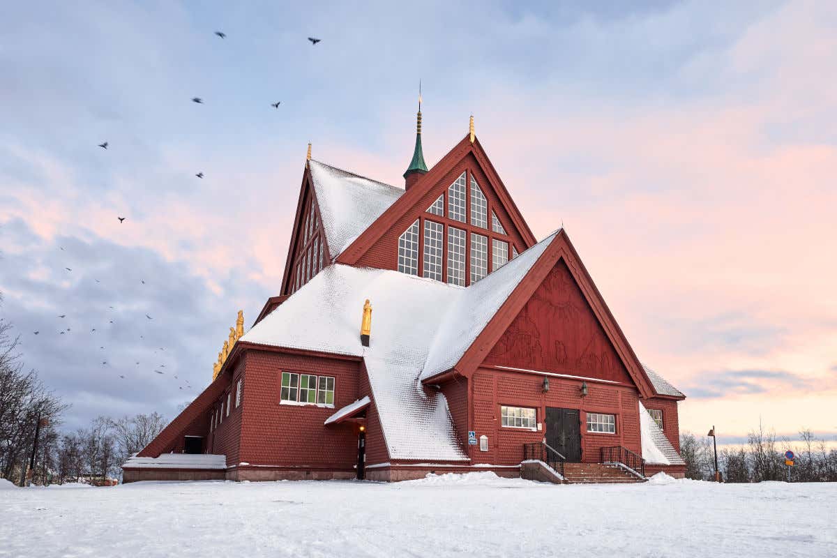 Una iglesia roja en mitad de la nada y rodeada por árboles en un paisaje nevado