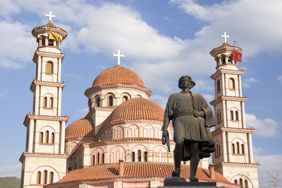 Esterno di una cattedrale con due torri e diversi piani con una scultura di un uomo in primo piano