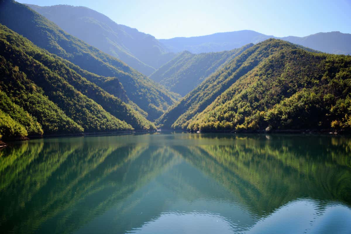 Un lago de aguas cristalinas y tonos esmeralda reflejando varias montañas de los alrededores