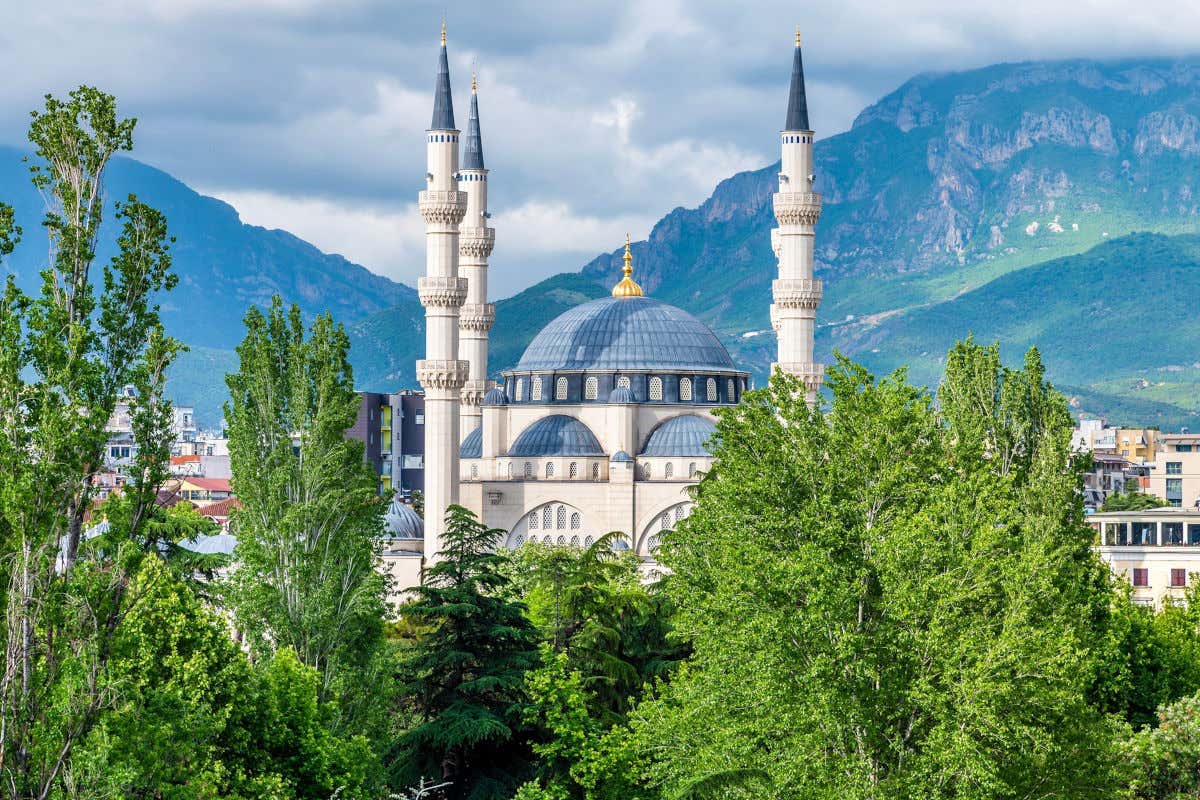 Una moschea con una grande cupola blu e quattro torri con delle montagne sullo sfondo