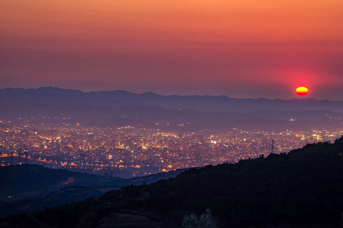 Il Monte Dajt al tramonto con il sole che cala all'orizzonte e gli edifici di Tirana illuminati