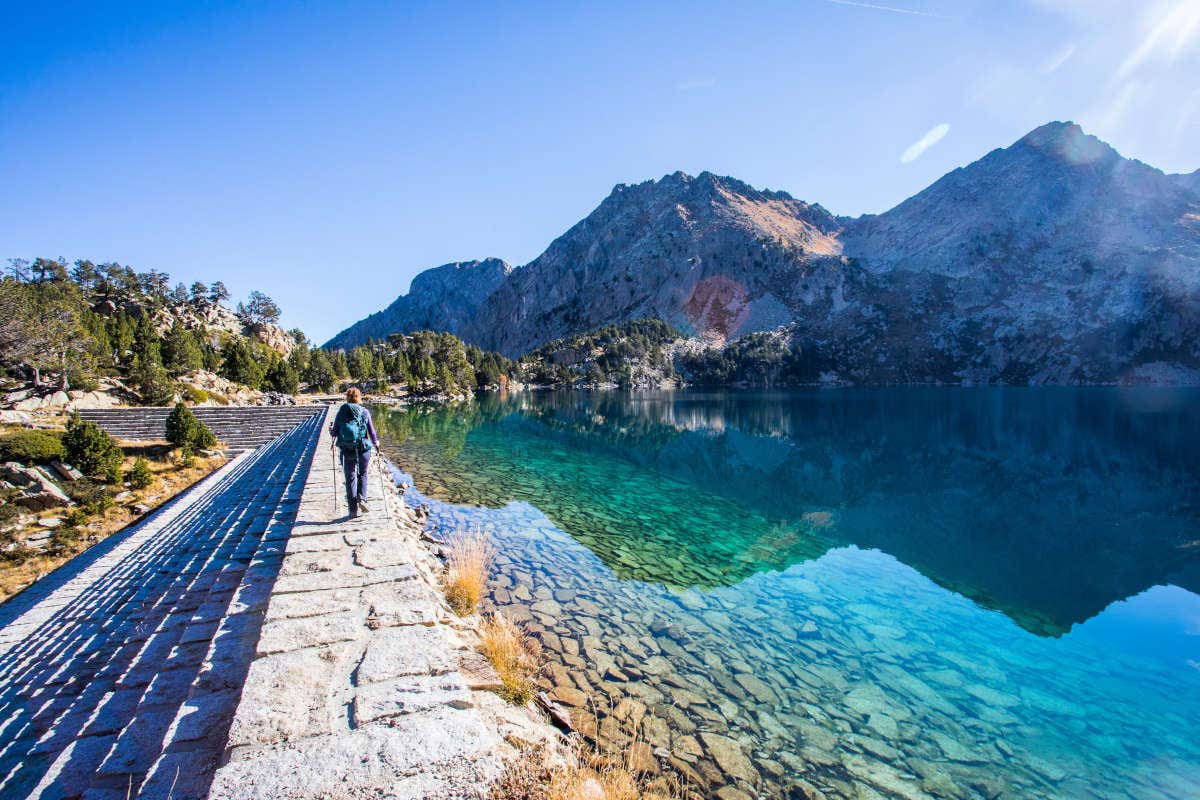 Una chica por un camino junto a un lago cristalino del Parque Nacional de Aigüestortes