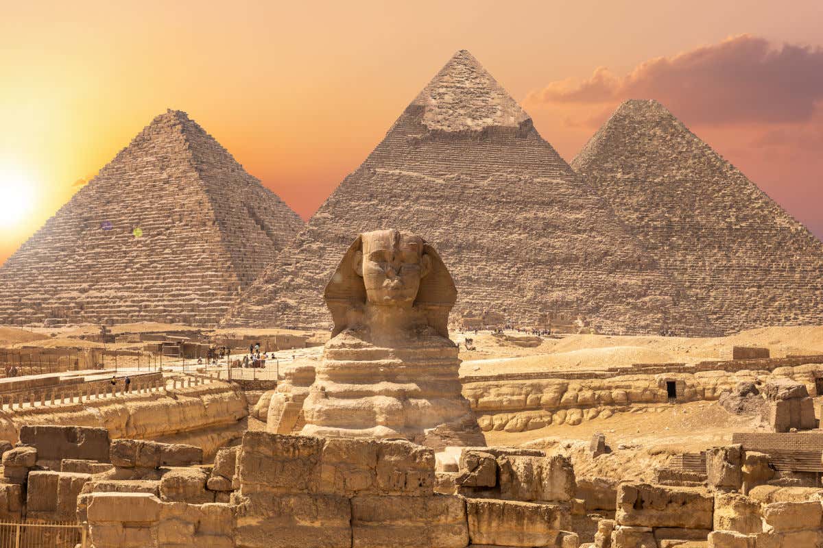 Panoramic view of the Pyramids of Giza with the Great Sphinx in the foreground and the sunset in the background.