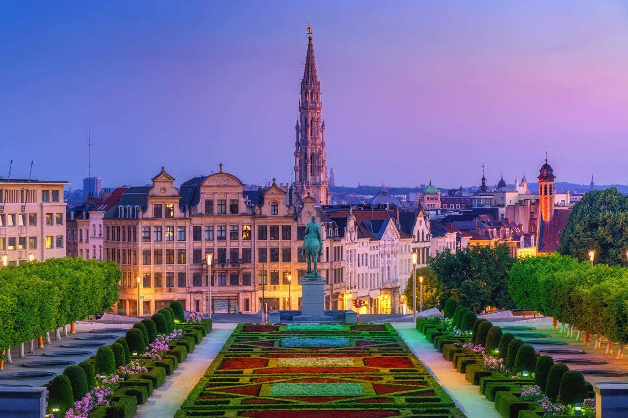 Jardins à la tombée de la nuit avec statue équestre au milieu et bâtiments en arrière-plan