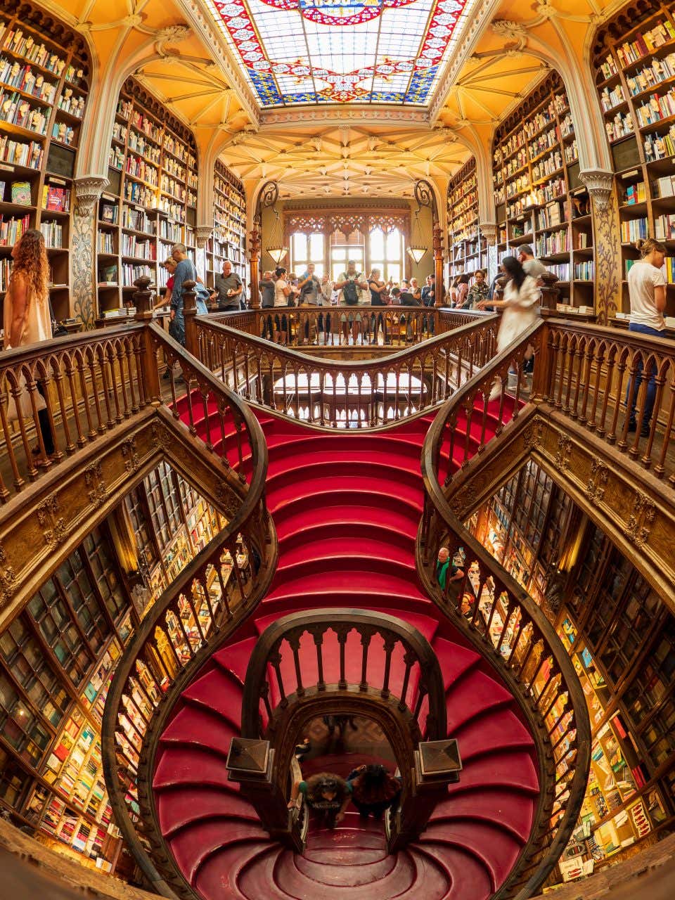 A busy bookshop with a red, curving staircase and ornate woodwork