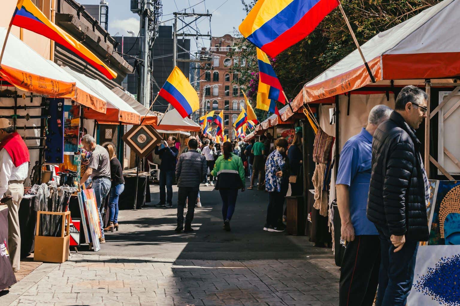 Strada affollata di persone con bancarelle su entrambi i lati e bandiere della Colombia in una giornata soleggiata