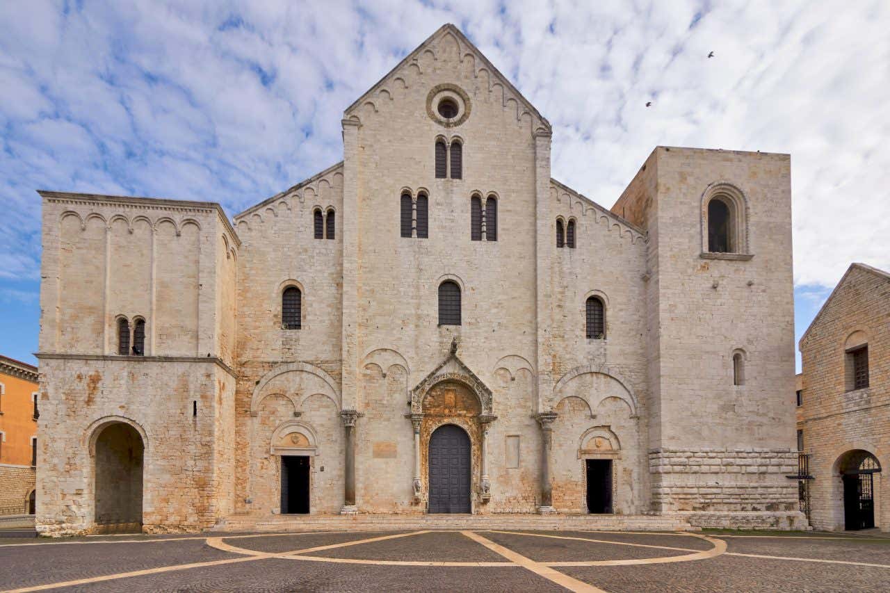 Una chiesa romanica in pietra bianca nel centro di Bari in Puglia, nella piazza circostante non ci sono persone e il cielo è coperto da nuvole