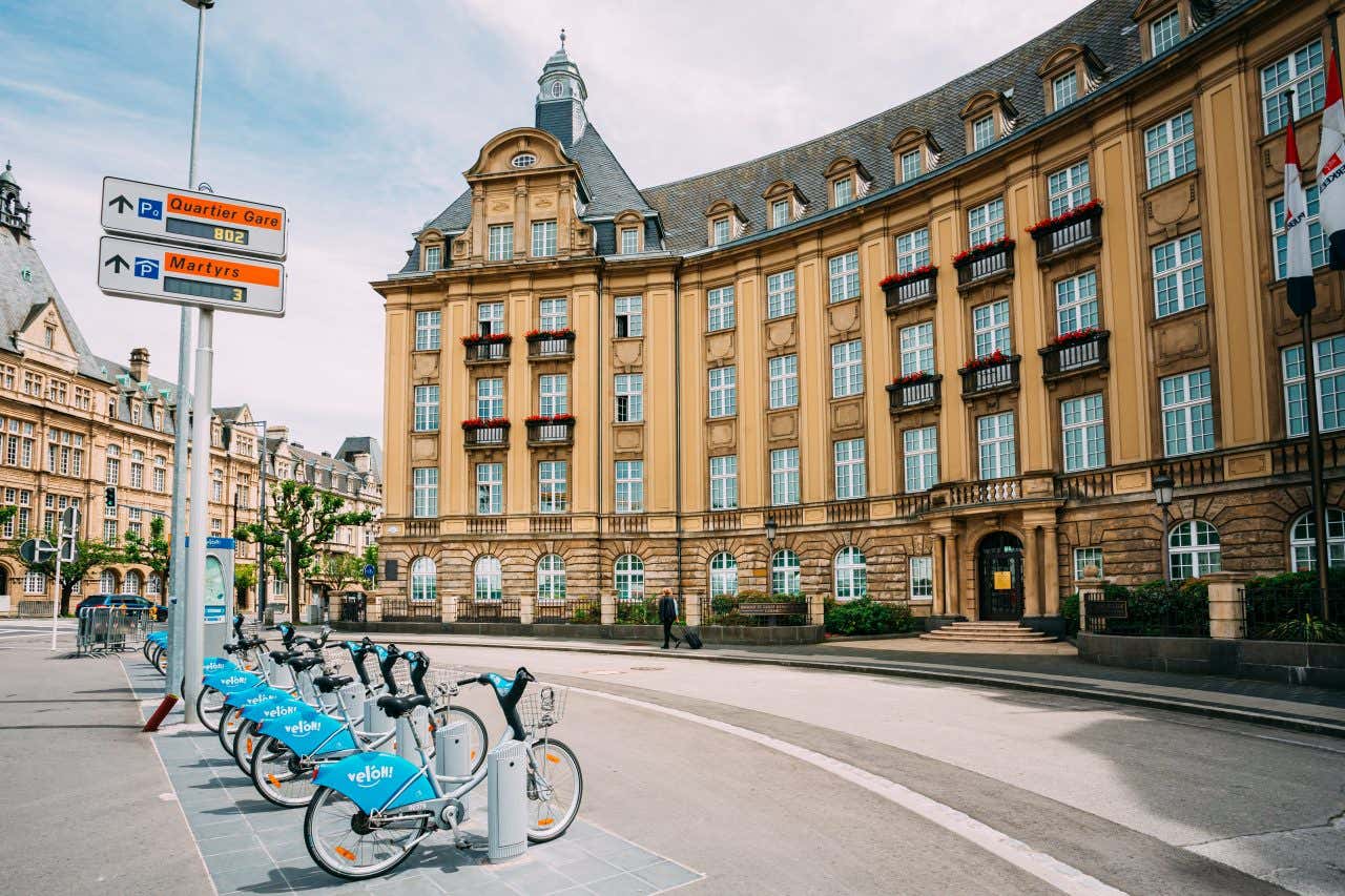 Electric bicycles called veloH in Luxembourg lined up at their parked station in a roundabout near a historic building