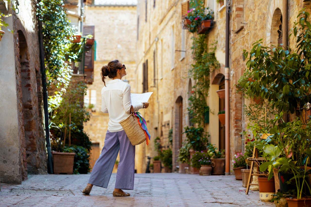 Una donna di spalle tra i vicoli del centro storico di Siena con in mano una cartina