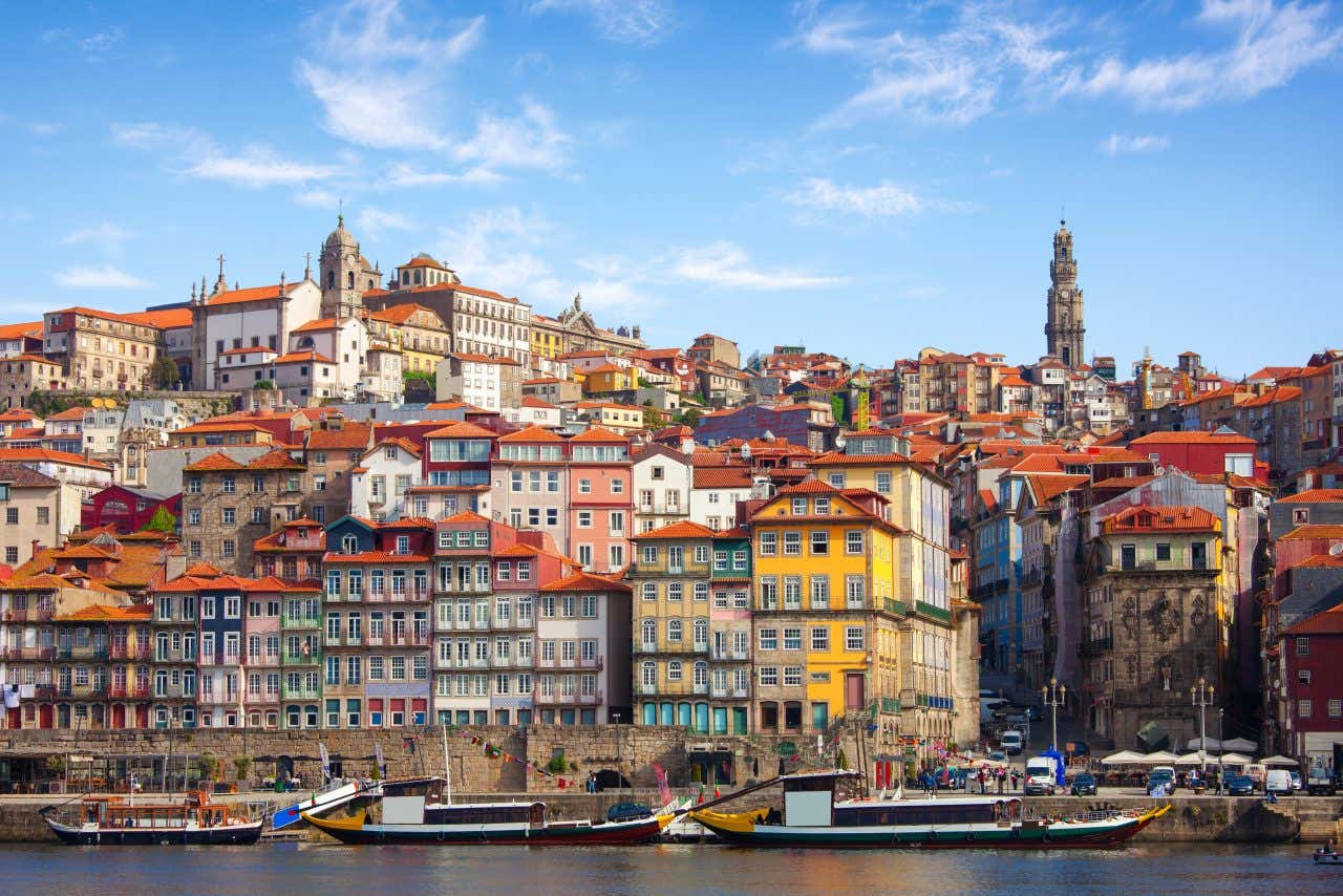 Many colorful and historic buildings in a city with a river and boats on a sunny day