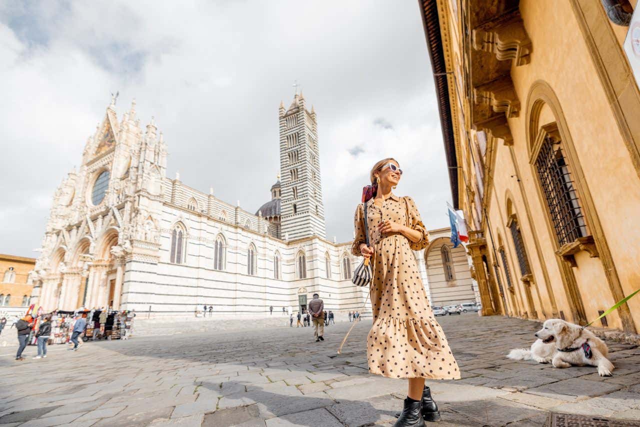 Una giovane donna in abiti estivi cammina per piazza Duomo, accanto all'imponente Duomo di Siena