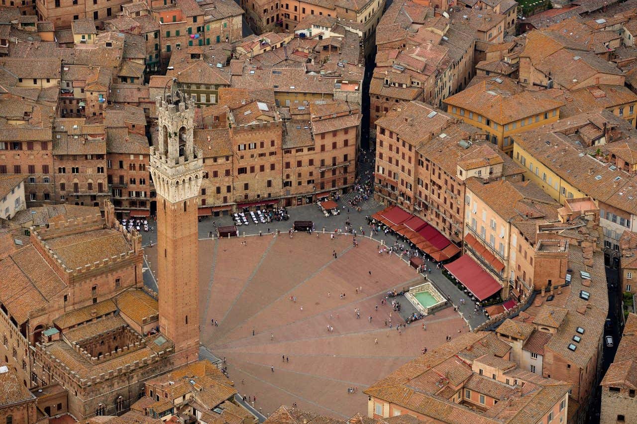 Il centro storico di Siena ripreso dall'alto, al centro una piazza a forma di ventaglio, un ovale semicircolare con alcune persone che passeggiano di giorno