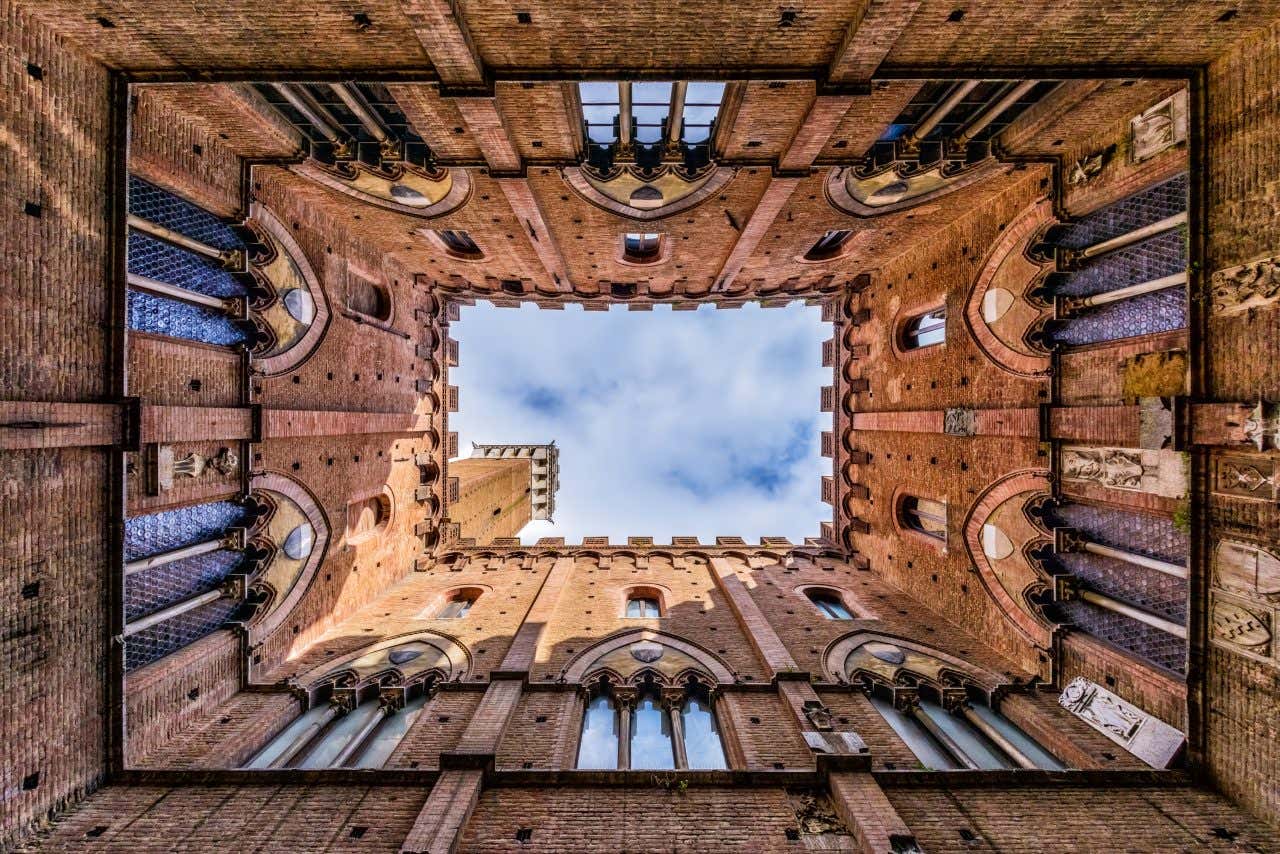 Le pareti del cortile interno del Palazzo Pubblico di Siena che incorniciano una porzione rettangolare di cielo e la cima della torre del mangia che spunta dall'angolo in basso a sinistra