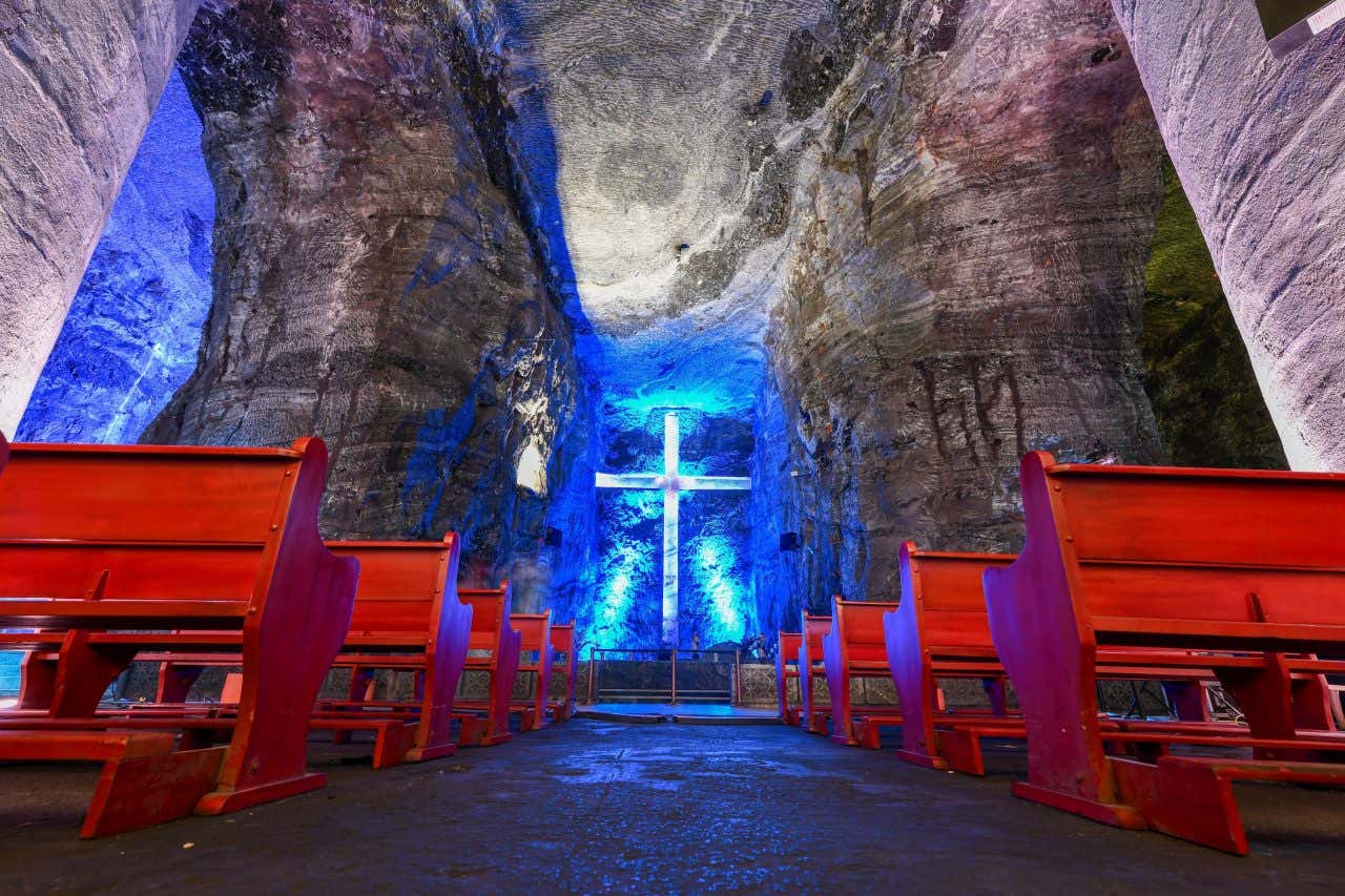 Catedral de Sal de Zipaquirá com bancos vermelhos e uma cruz iluminada de azul ao fundo