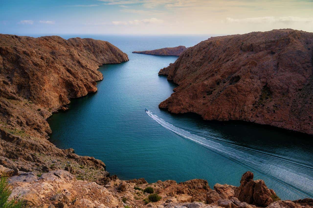 Un fiordo in Oman circondato da rocce rossastre e una barca che lo attraversa