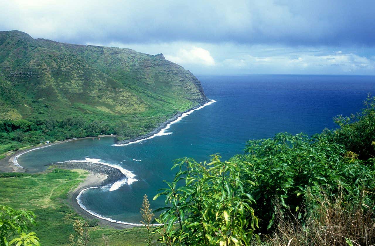 An aerial view of Moloka'i's curvey coastline and green mountains in the background.