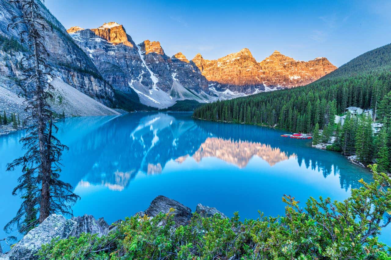 Lac bleu turquoise entouré de montagnes enneigées et de forêt de sapins sous un ciel dégagé