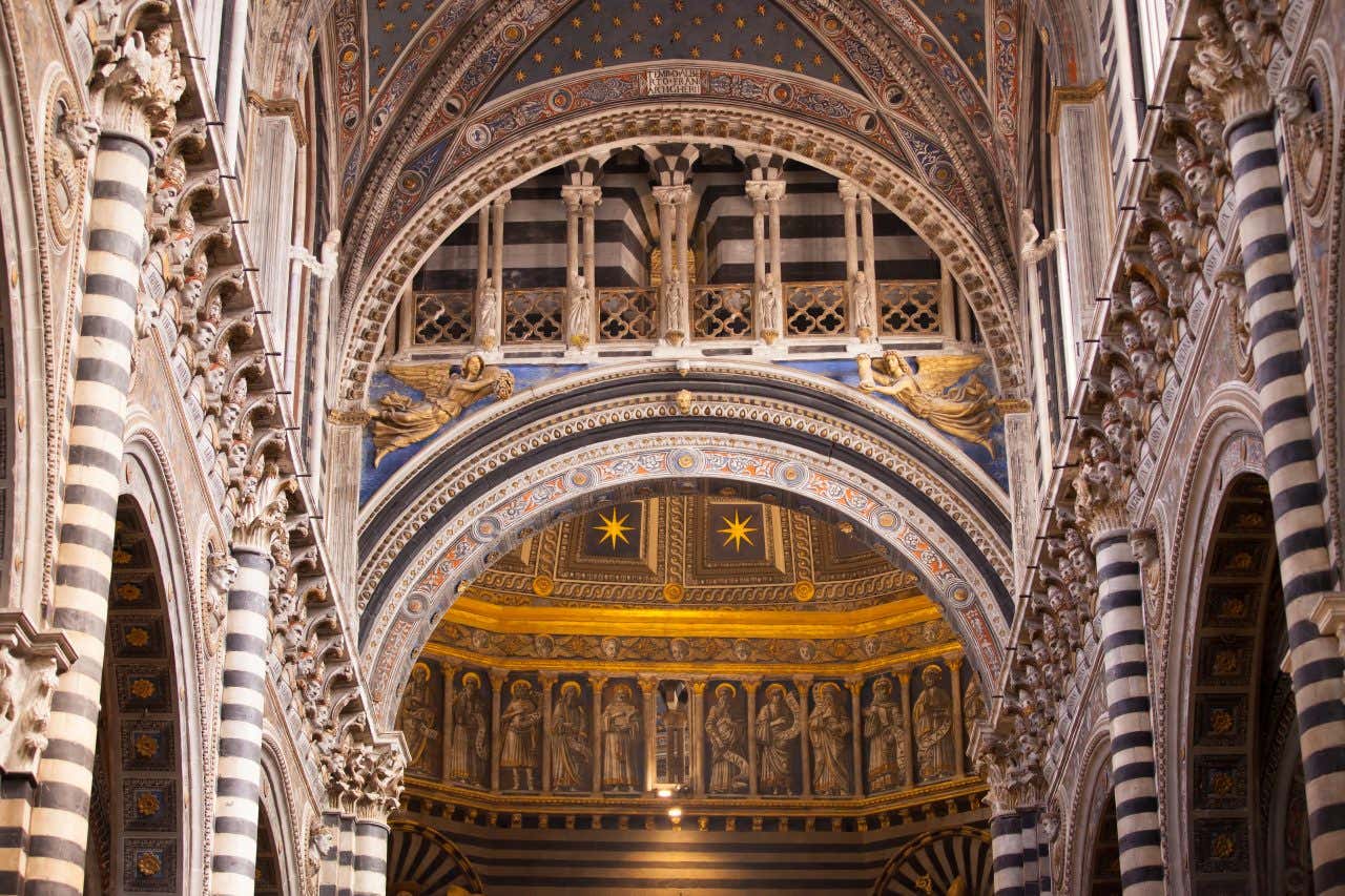 Colonnati, archi, sculture di angeli in legno dorato, affreschi e busti di santi disposti sulla parte superiore dell'interno della cattedrale di Siena