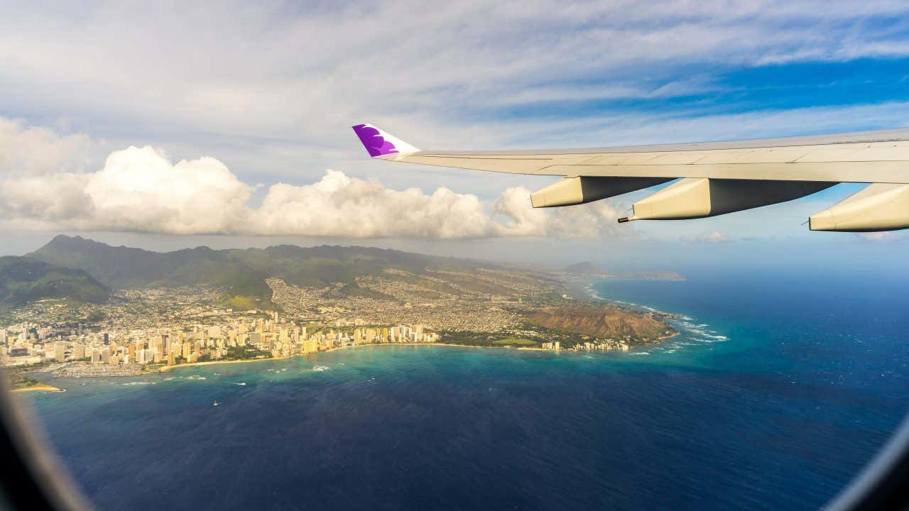 Views from a plane over Oahu, with the ocean and the cloudy sky in view.