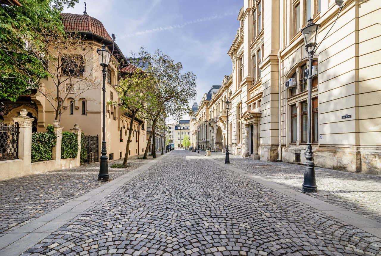 Una strada acciottolata con dei lampioni ai lati e palazzi in stile liberty nel centro di Bucarest