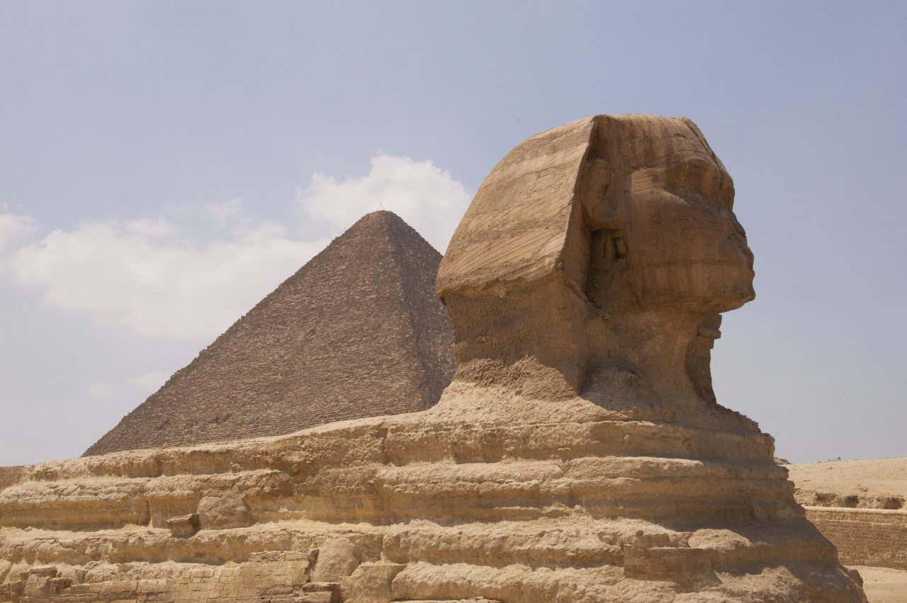 I resti della sfinge in primo piano e una piramide in pietra sullo sfondo in una giornata di sole al Cairo