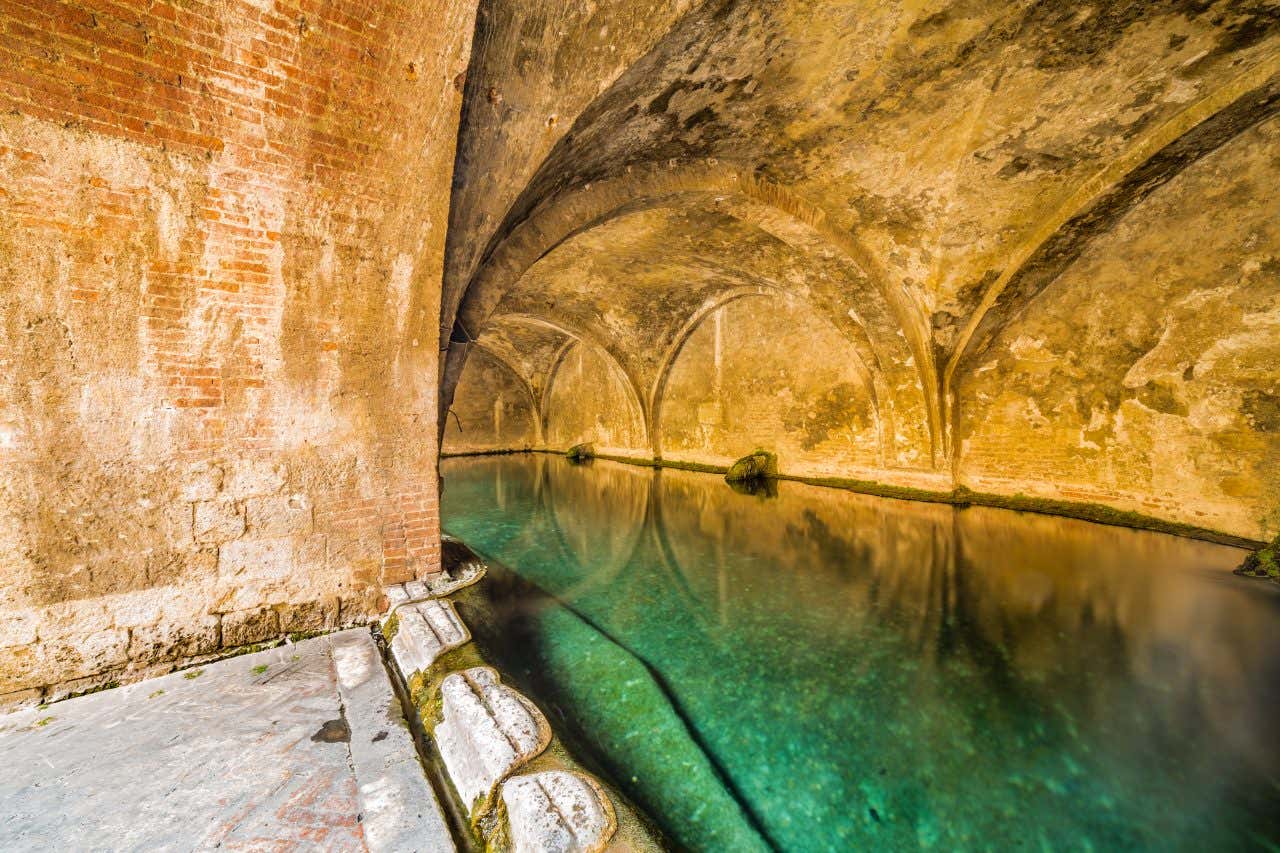 Una grande vasca di acqua piovana trasparente, sormontata da ampie arcate gotiche in pietra e mattoni