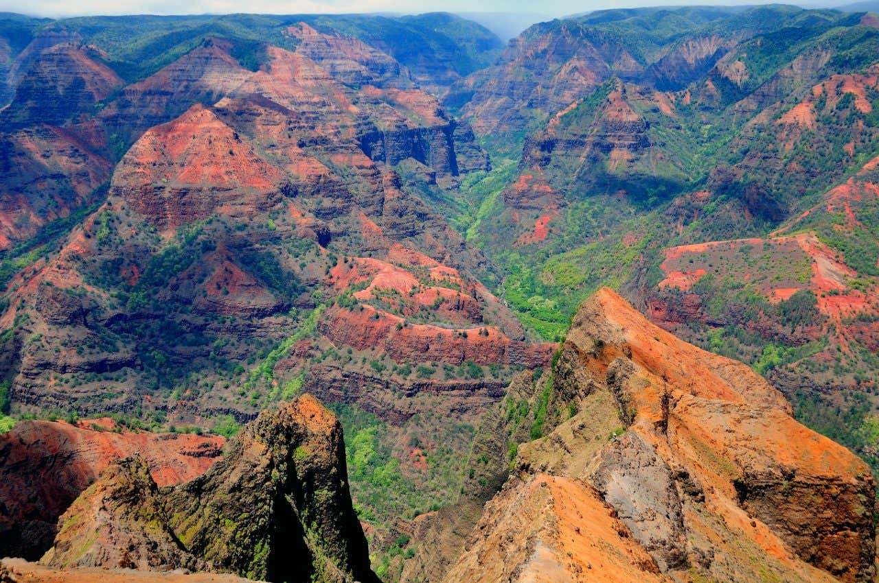 An aerial shot of Waimea Canyon, with green and orange hues defining the mountains.