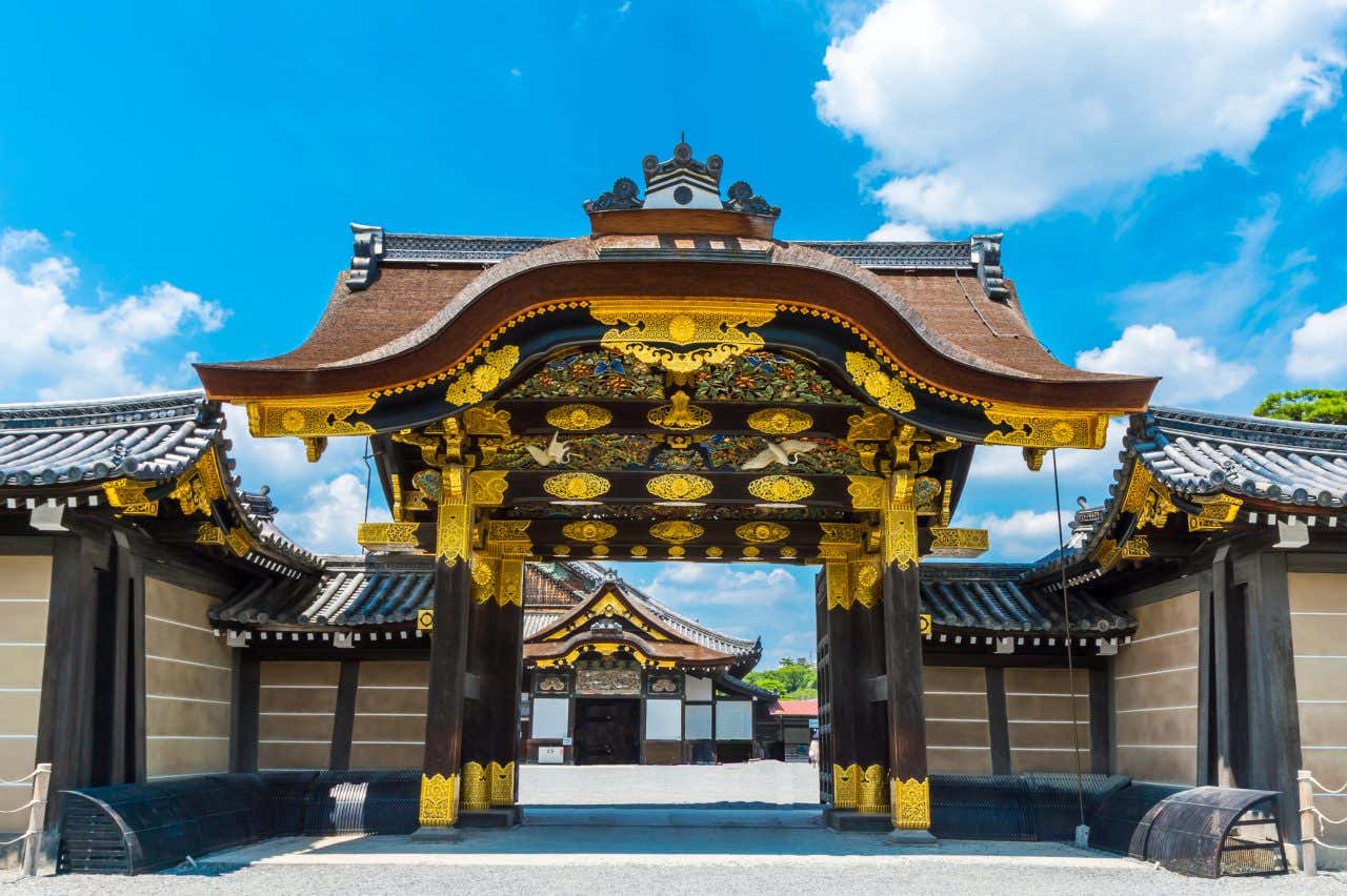 The gates of Nijo Castle, with distinctive black and yellow colors and a cloudy blue sky in the background.