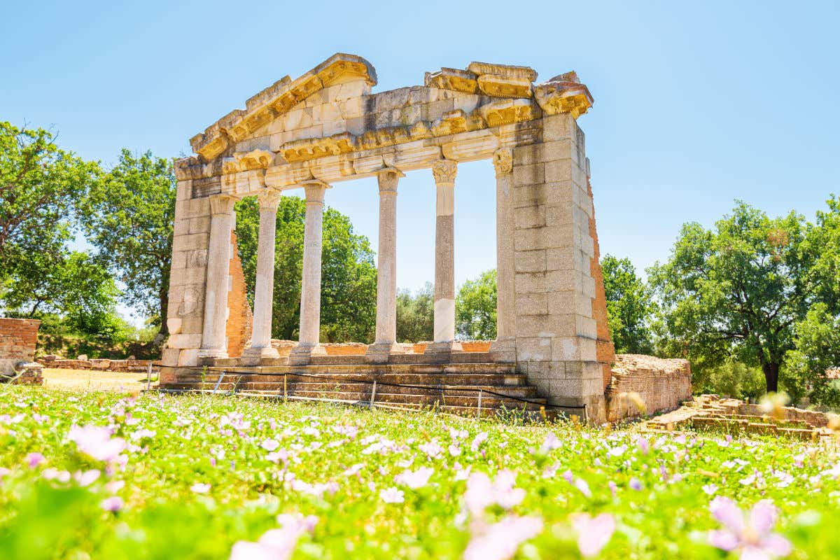 Ruinas de un templo de estilo griego clásico rodeado por césped, árboles y algunas flores