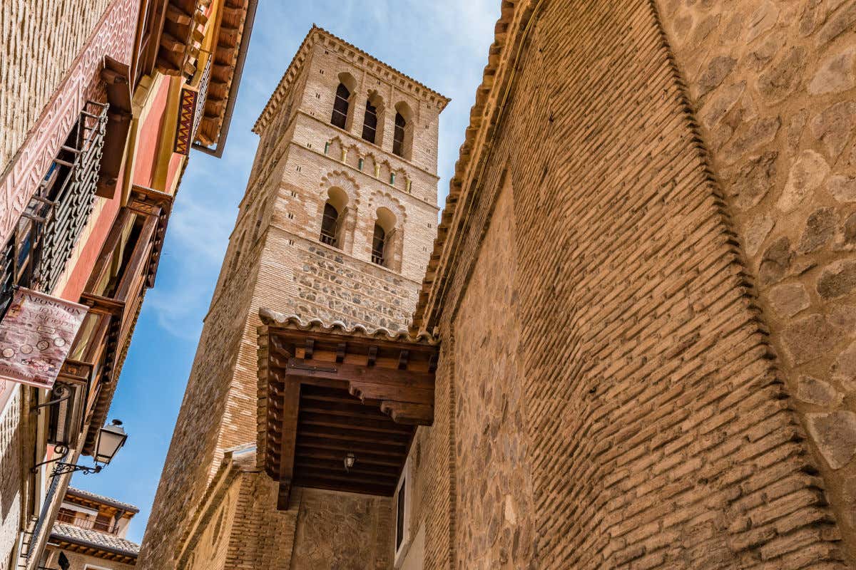 Torre de una iglesia de piedra de aspecto mudéjar en una estrecha callejuela