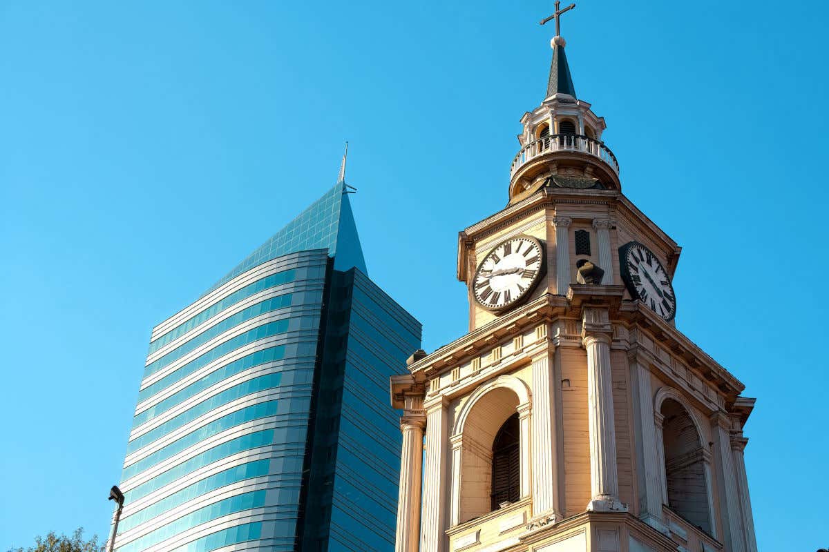 Torre de la iglesia de San Francisco con sus relojes junto a un moderno rascacielos en Santiago de Chile