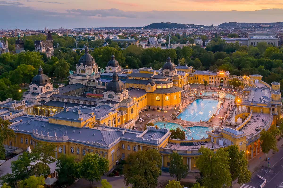 Vista aérea de las piscinas exteriores del balneario Széchenyi rodeadas de árboles y de unos edificios clásicos de tonos amarillos