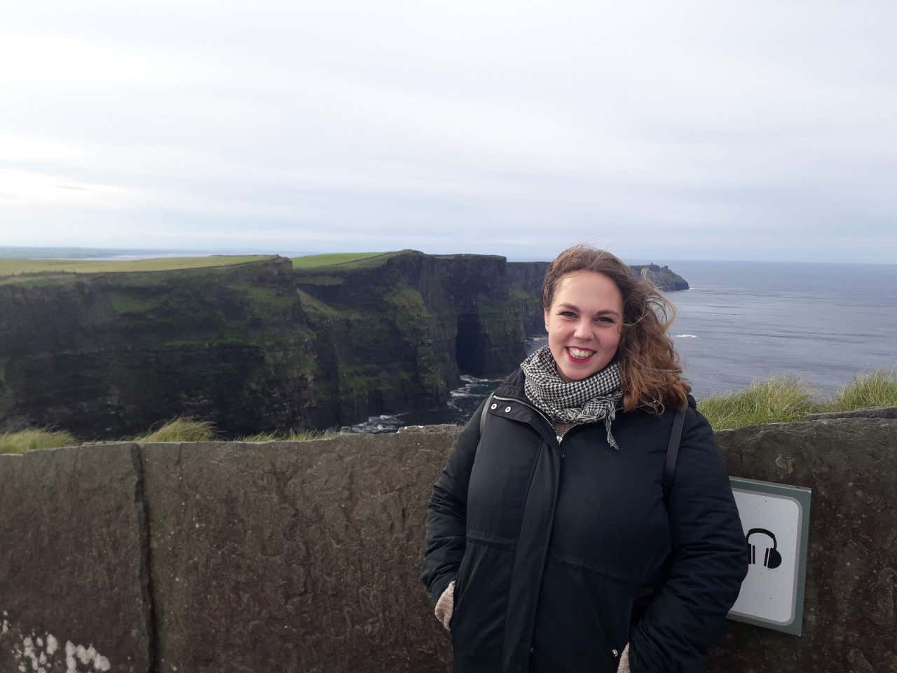 Chica posando para una foto con los acantilados de Moher de fondo en un día gris